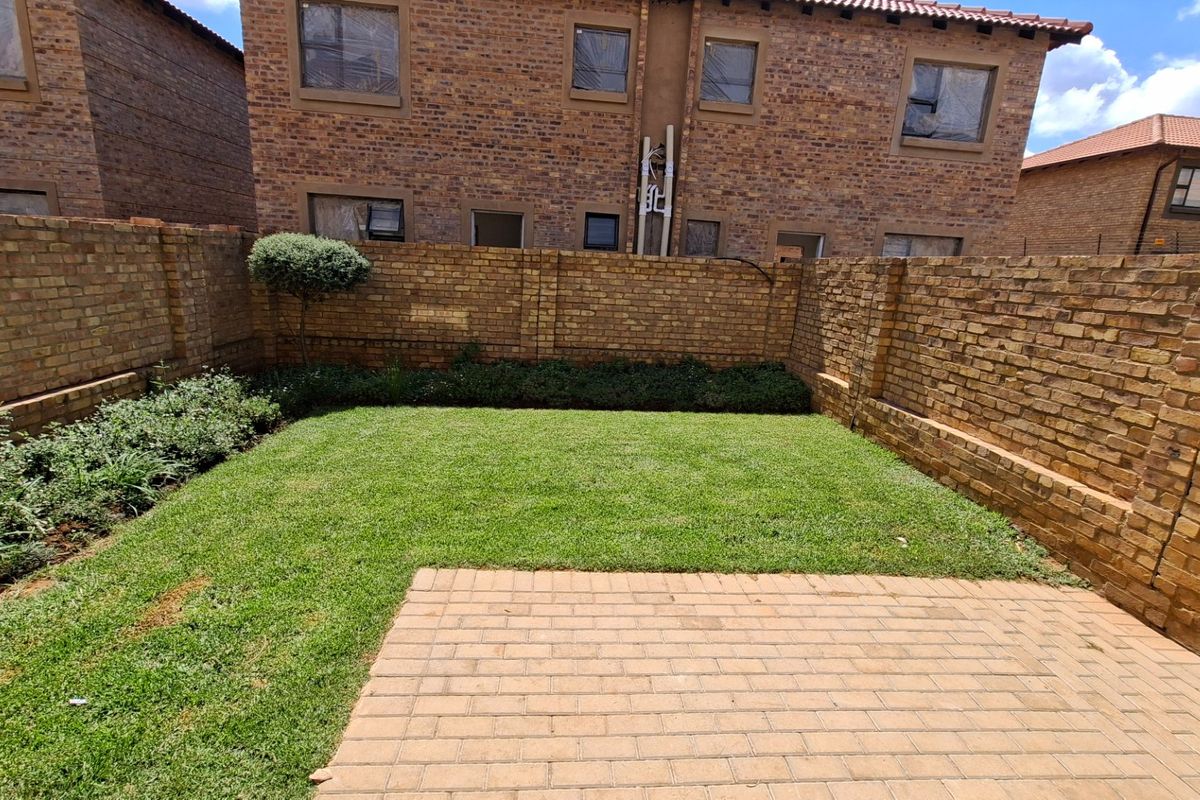 A private rear garden featuring a paved patio area, well-maintained lawn, and established brick boundary walls.