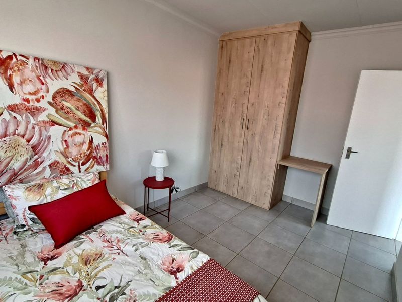 A bedroom featuring tiled flooring, a built-in wooden wardrobe with an integrated desk, and coved ceiling detailing.