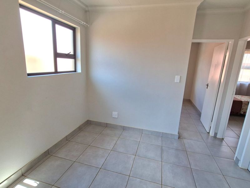 A bright, empty bedroom featuring neutral tiled flooring and a large window, providing a clean canvas for personalization.