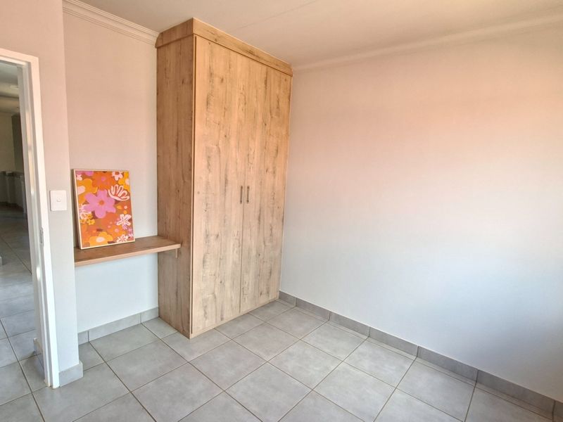 A clean, neutral bedroom featuring light wood-finish built-in wardrobes and durable tiled flooring, offering a bright and versatile space.