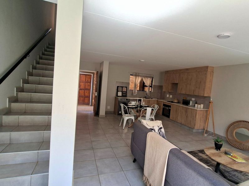 Open-plan living area featuring a modern kitchen with wood-finish cabinetry, tiled flooring throughout, and a staircase leading to the upper level.