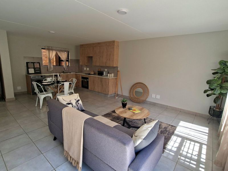 Open-plan living area featuring a modern kitchen with wood-look cabinetry, built-in oven, and tiled flooring throughout, creating a functional and cohesive space.