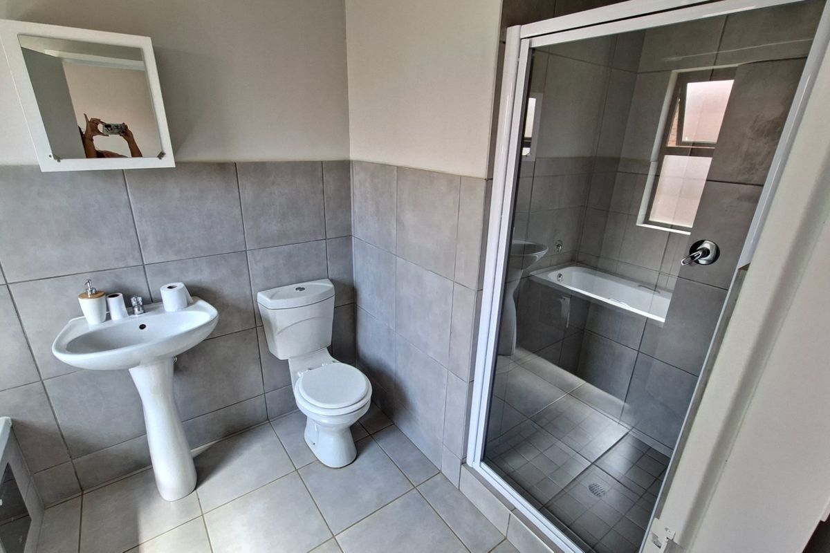 A clean, modern bathroom featuring a pedestal basin, toilet, separate shower enclosure, and a bathtub with neutral grey wall and floor tiling.