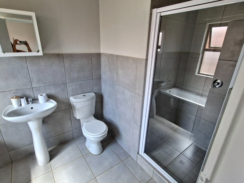 A clean, modern bathroom featuring a pedestal basin, toilet, separate shower enclosure, and a bathtub with neutral grey wall and floor tiling.
