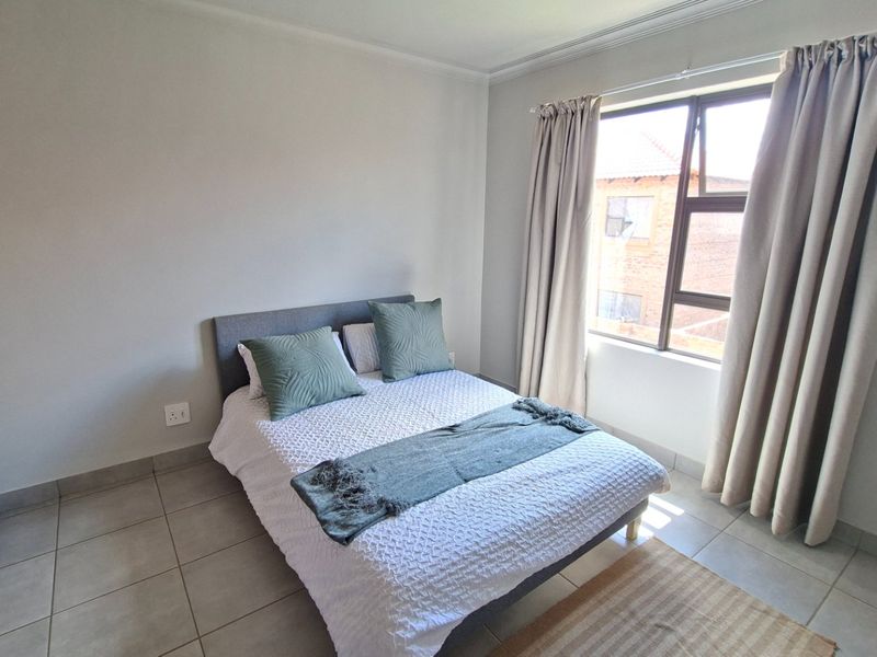 A well-maintained bedroom featuring neutral tiled flooring, a built-in wardrobe, and a large window allowing for natural light.