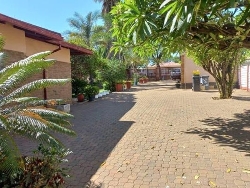 A paved driveway leading towards the front of the property, featuring established trees and brick exterior wall finishes.