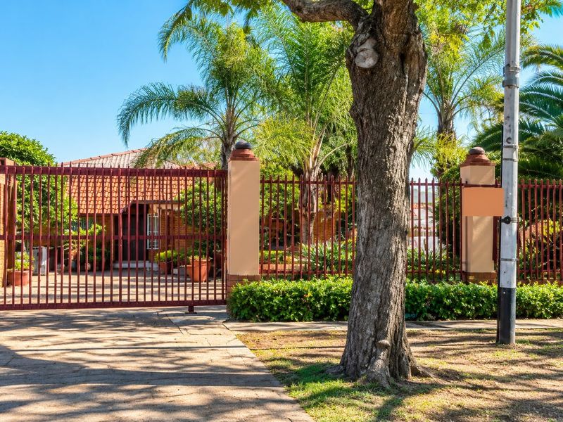 Front view of the property featuring a secure metal gate, brick pillars, and a paved driveway entrance.