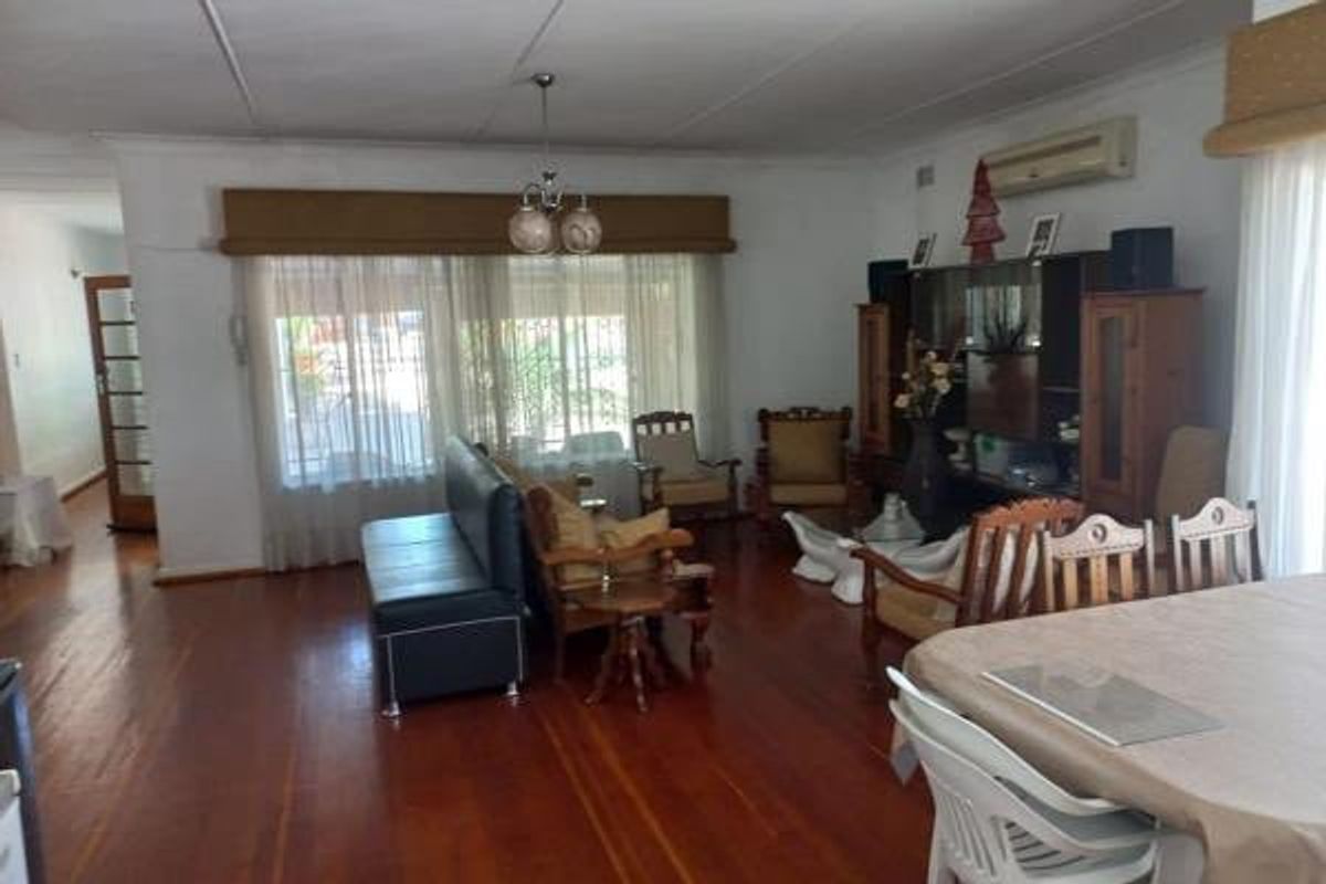 Spacious living area featuring polished hardwood flooring, a split-system air conditioner, and large windows with fitted pelmets, offering a comfortable and functional layout.
