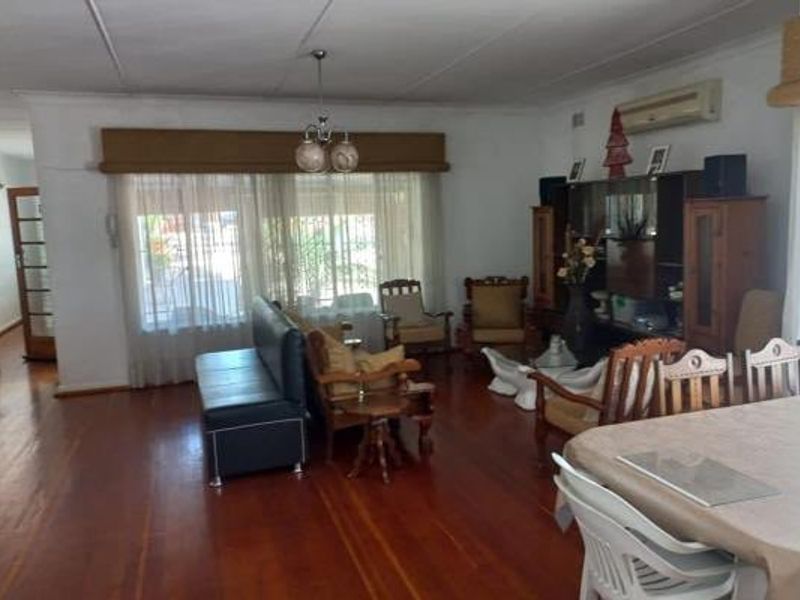 Spacious living area featuring polished hardwood flooring, a split-system air conditioner, and large windows with fitted pelmets, offering a comfortable and functional layout.