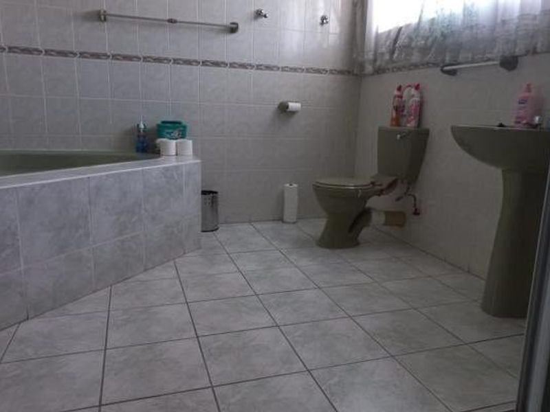 A functional bathroom featuring a built-in corner bathtub, pedestal sink, and toilet with neutral tiled finishes throughout.