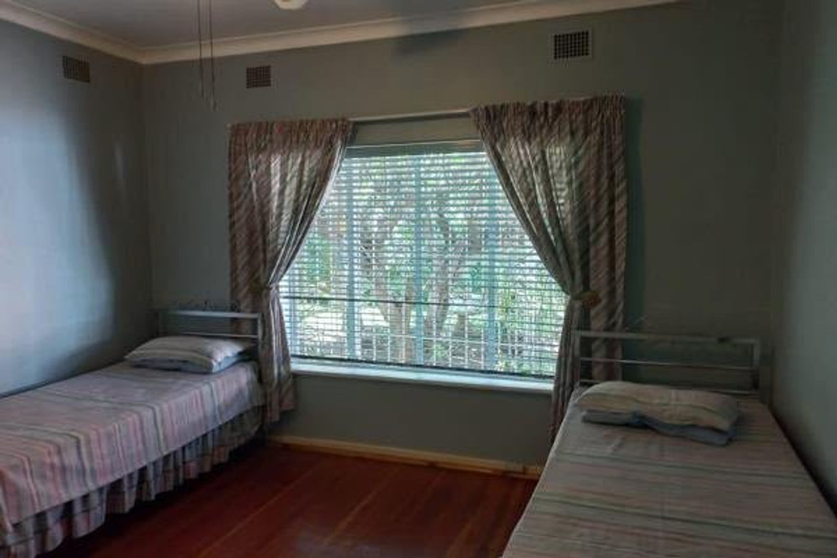 A bedroom featuring polished timber flooring, a large window with venetian blinds, and decorative ceiling cornicing.