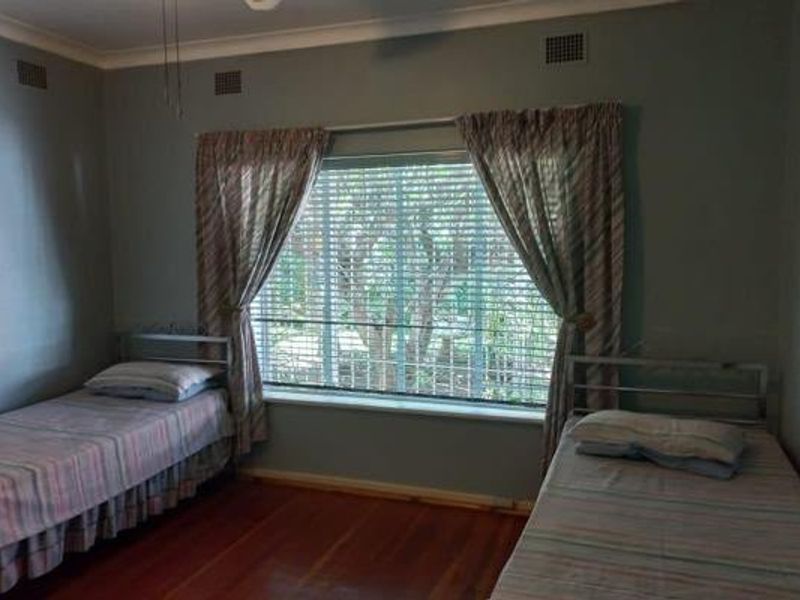 A bedroom featuring polished timber flooring, a large window with venetian blinds, and decorative ceiling cornicing.