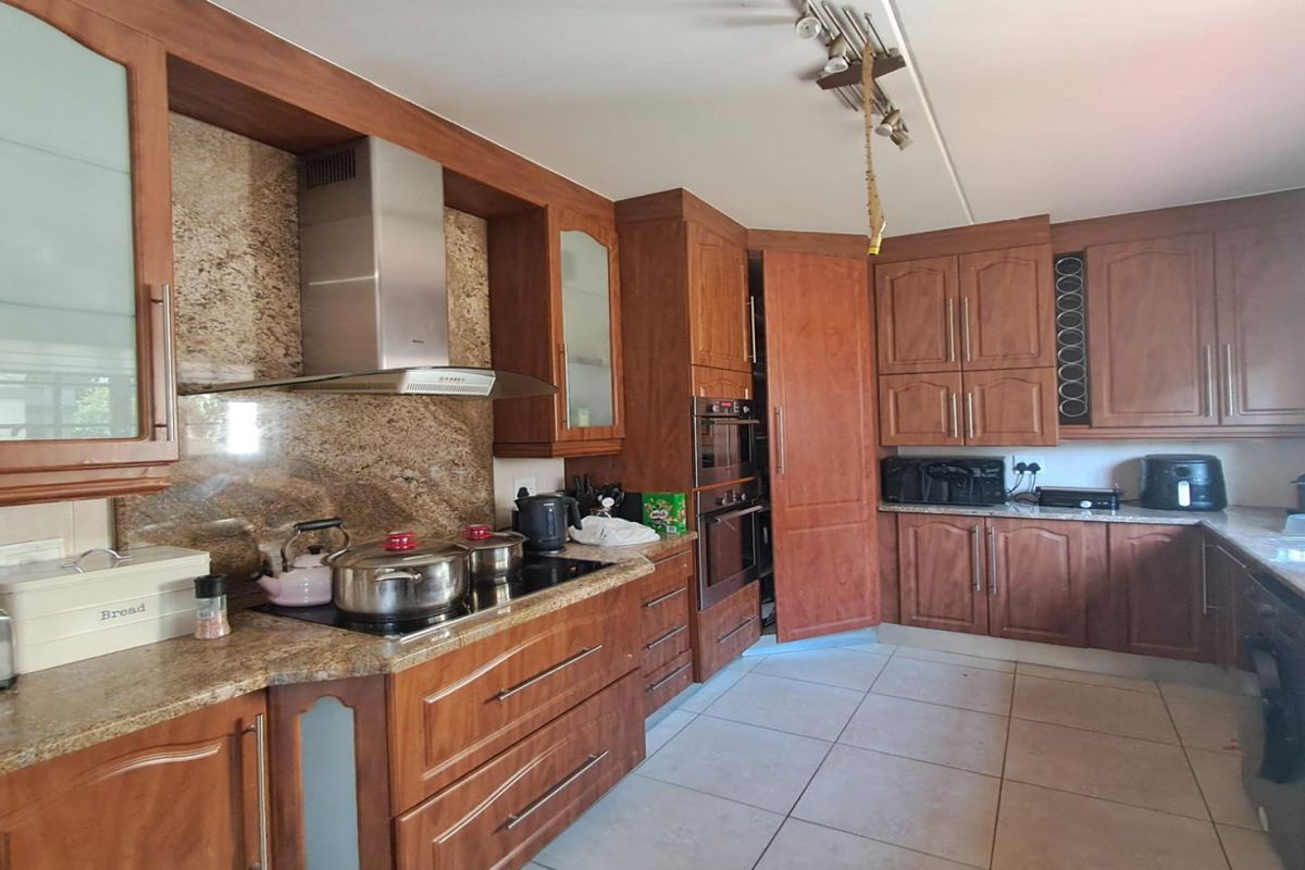 A functional kitchen featuring wooden cabinetry, granite countertops, built-in oven, and extractor fan with tiled flooring.