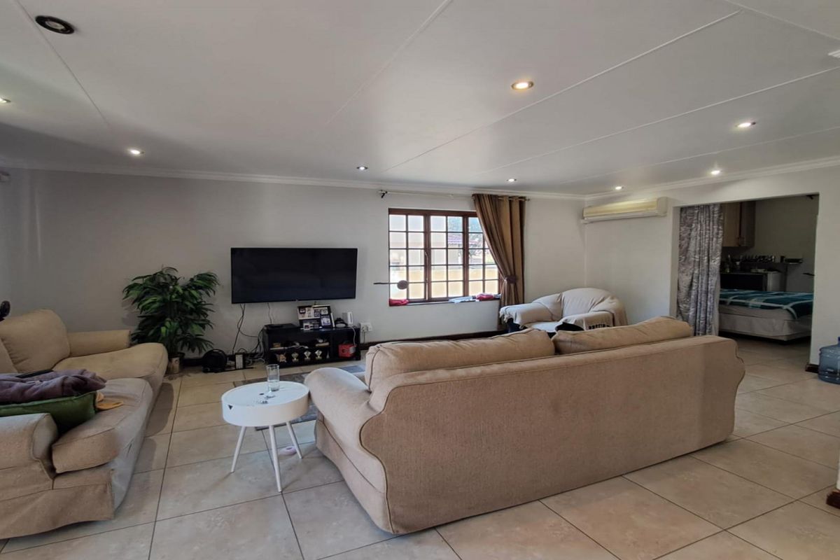 Spacious living room featuring tiled flooring, recessed downlighting, and an integrated air conditioning unit, with an adjacent view into a secondary room.