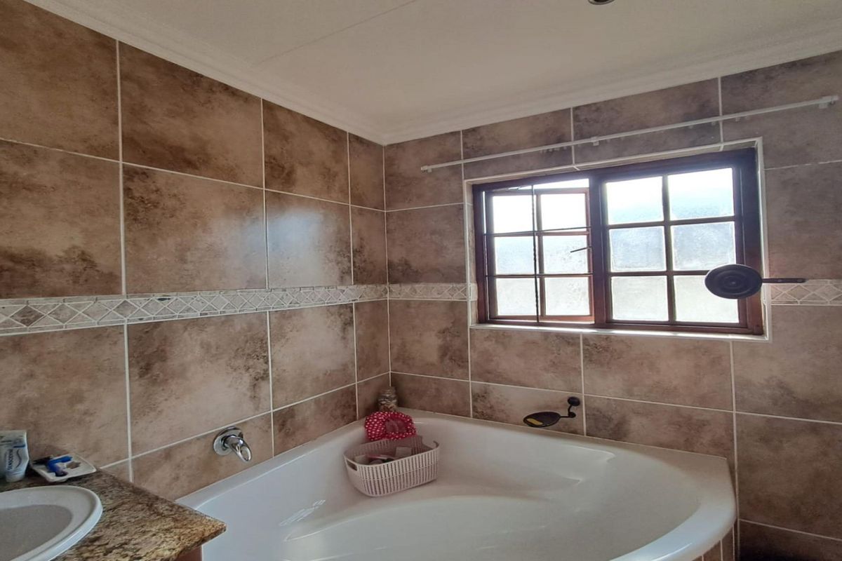 A bathroom featuring a corner bathtub, tiled walls, and a granite vanity countertop with a built-in basin.