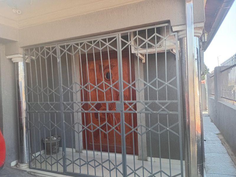 A secure entrance area featuring a decorative wooden front door, protected by a metal security gate, with an integrated air conditioning unit.