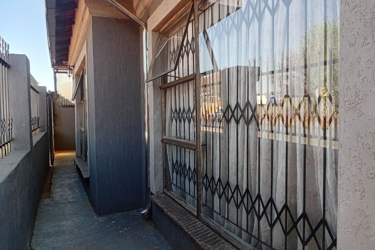 A narrow side passage of the house featuring a concrete walkway, security gates on windows, and a boundary wall.