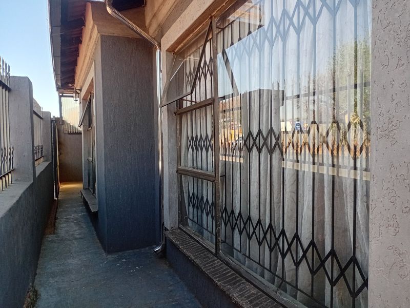 A narrow side passage of the house featuring a concrete walkway, security gates on windows, and a boundary wall.