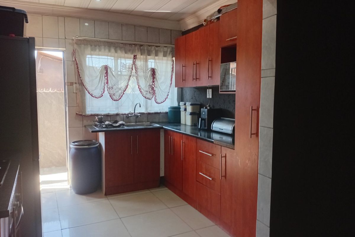 A functional kitchen featuring wood-tone cabinetry, dark laminate countertops, tiled flooring, and a tiled backsplash with direct access to an exterior area.