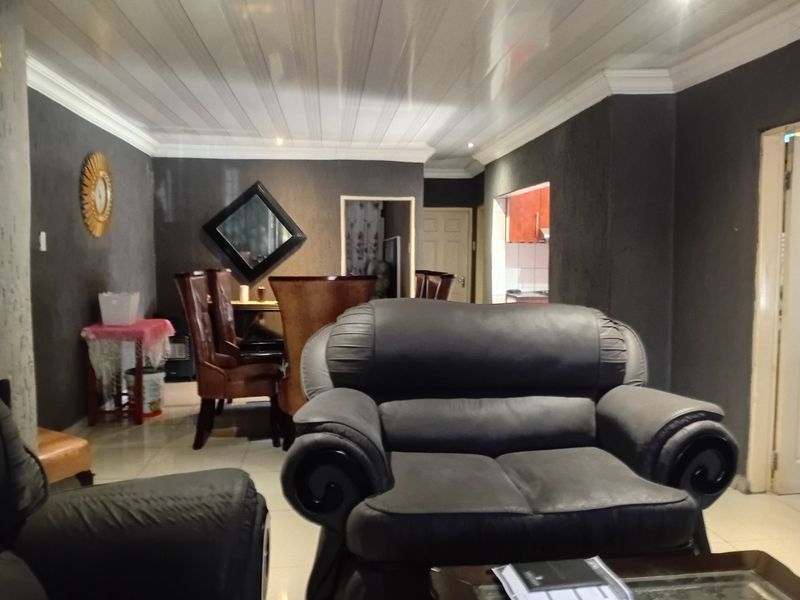 A living room area featuring tiled flooring and a glossy panelled ceiling, with an open layout leading towards the kitchen area.