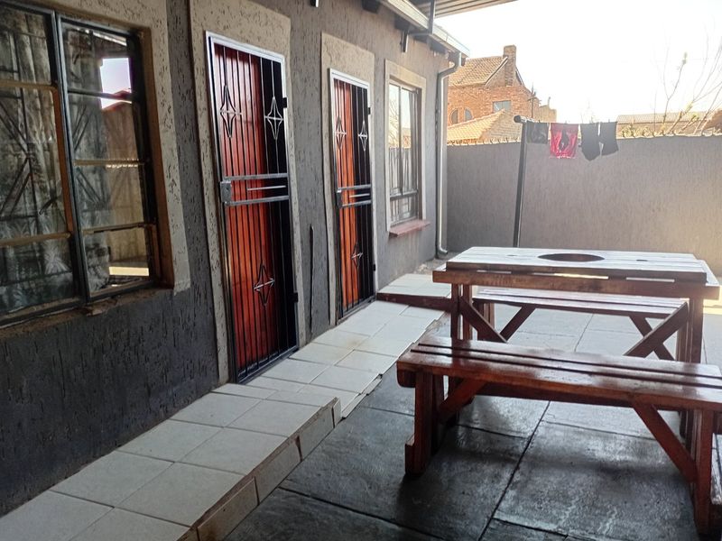 A covered patio area featuring tiled flooring, security gates on external doors, and textured wall finishes, providing a functional outdoor space.
