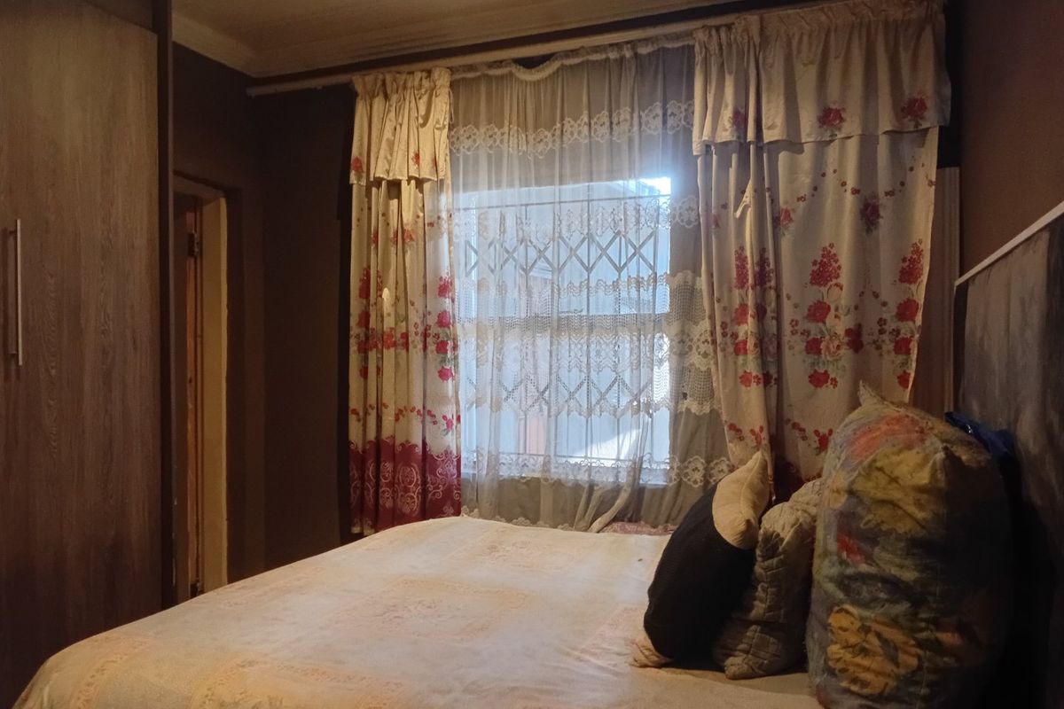 A bedroom featuring built-in cupboards and a window fitted with a security gate.