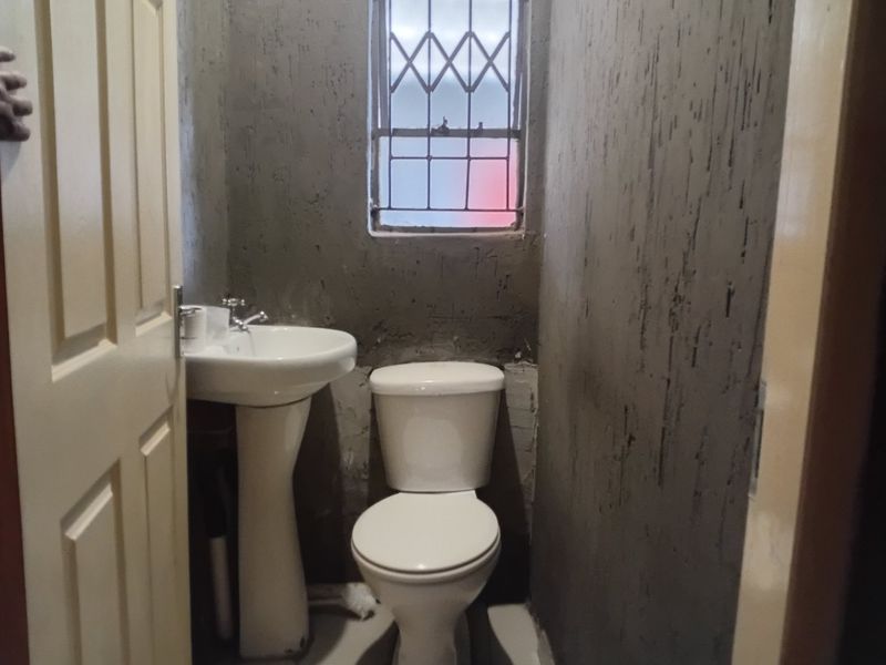 A small bathroom featuring a pedestal basin and toilet, currently in an unfinished state with exposed plaster walls.