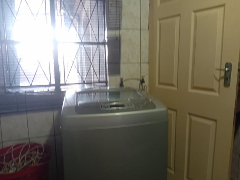 A functional laundry area featuring tiled walls, a window with security bars, and a standard interior door.