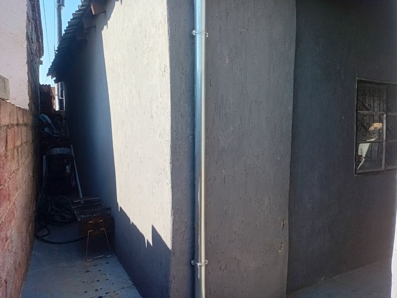 Side exterior view of the property featuring a textured plaster finish, metal downpipe, and window with security bars.