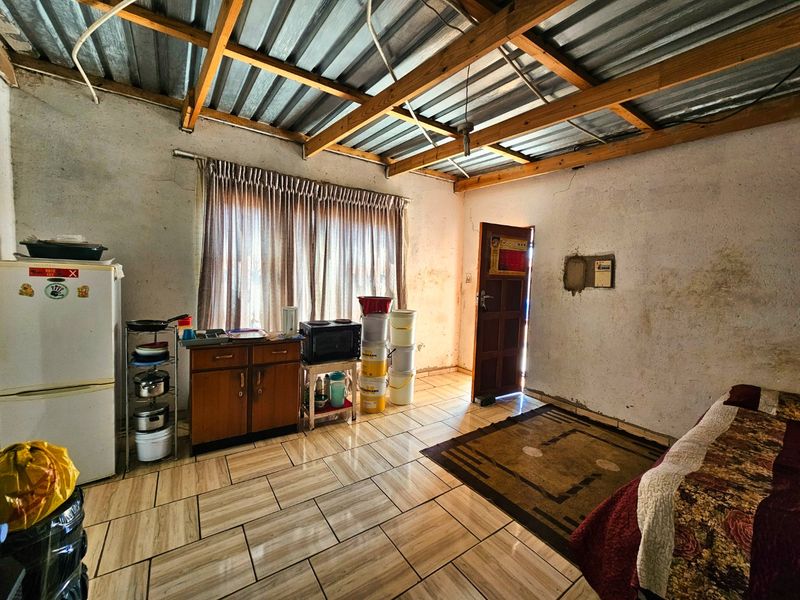 Open plan living area featuring exposed timber roof trusses, corrugated metal ceiling, and tiled flooring, requiring cosmetic updates to wall finishes.