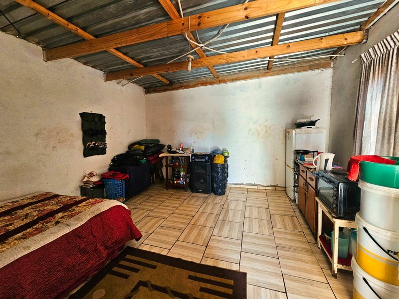 Open plan living area featuring ceramic floor tiles and exposed timber roof trusses with corrugated metal ceiling.