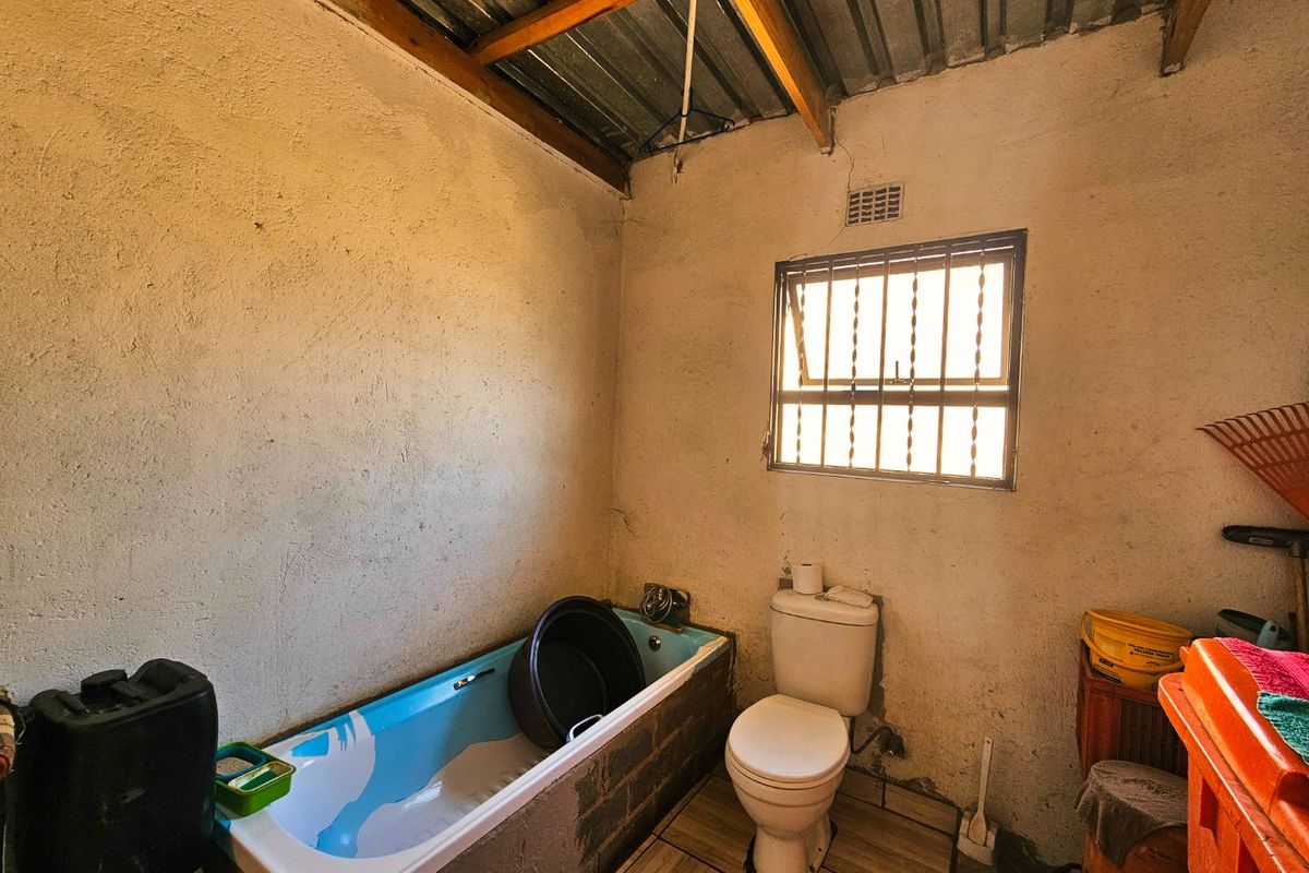 A basic bathroom featuring a bathtub, toilet, tiled flooring, and a window with security bars, requiring significant cosmetic updates and finishing work.