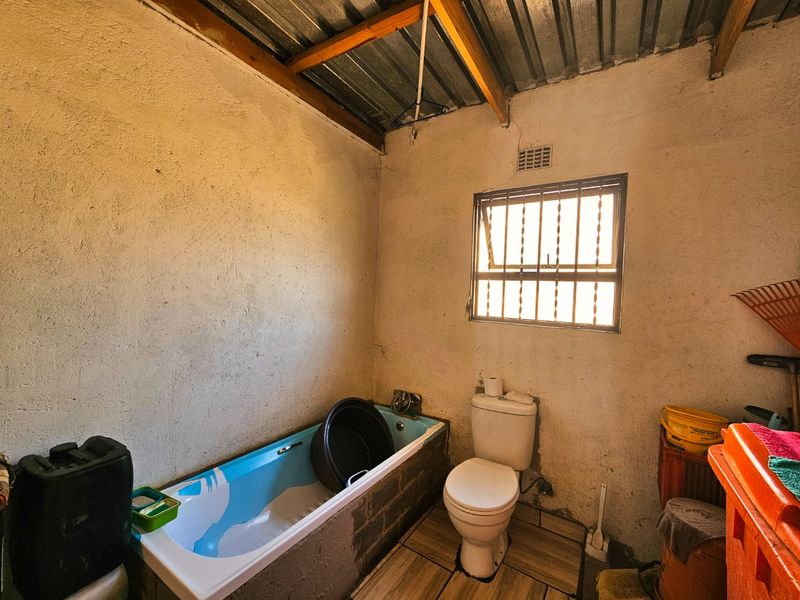 A basic bathroom featuring a bathtub, toilet, tiled flooring, and a window with security bars, requiring significant cosmetic updates and finishing work.