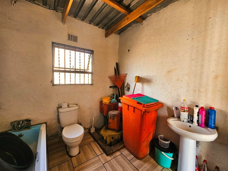 A basic bathroom featuring a pedestal basin, toilet, and bathtub with tiled flooring and exposed roof rafters, requiring significant renovation and cosmetic updates.