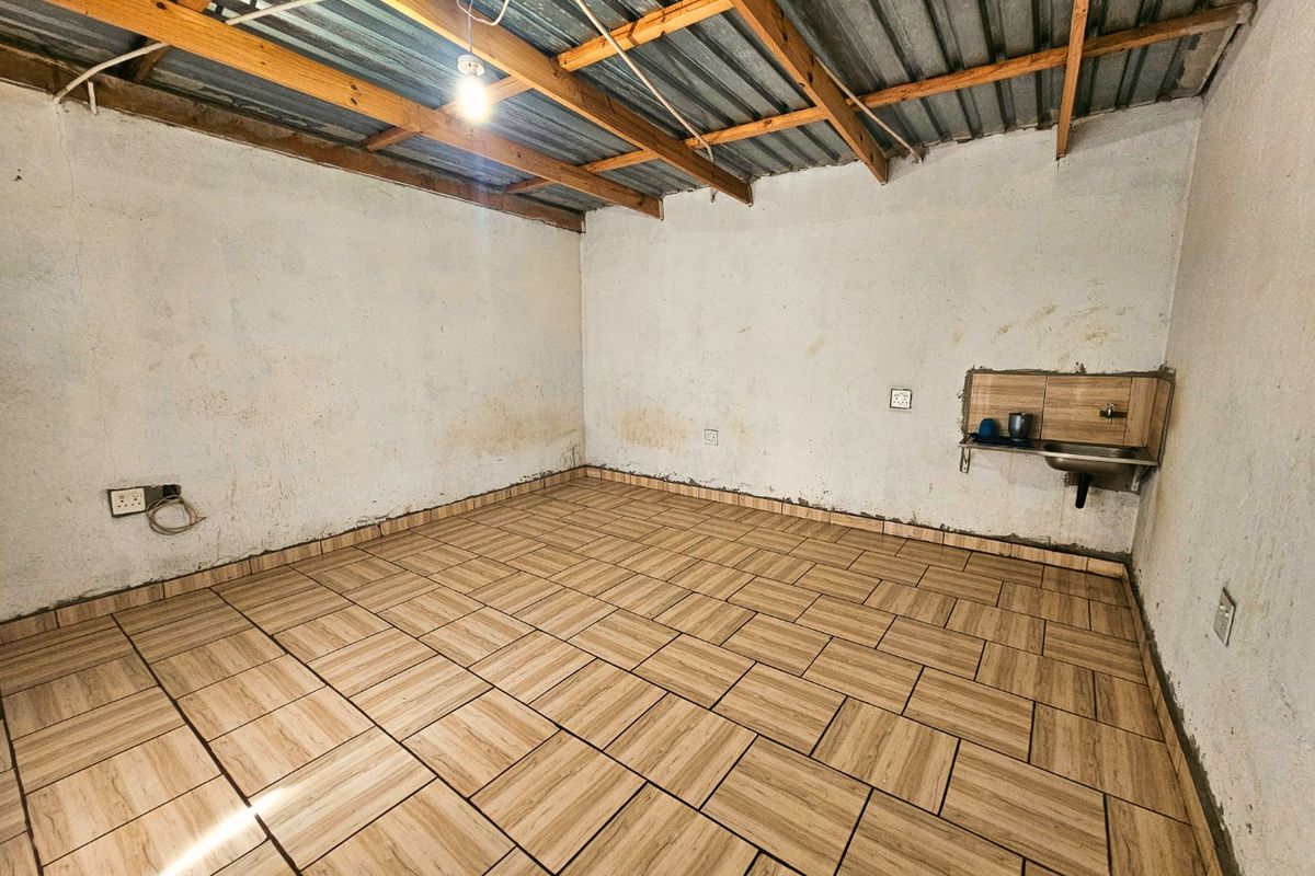 An unfinished utility space featuring exposed timber roof trusses, tiled flooring, and a basic wall-mounted sink, suitable for renovation or storage use.
