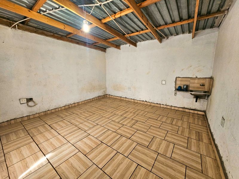 An unfinished utility space featuring exposed timber roof trusses, tiled flooring, and a basic wall-mounted sink, suitable for renovation or storage use.