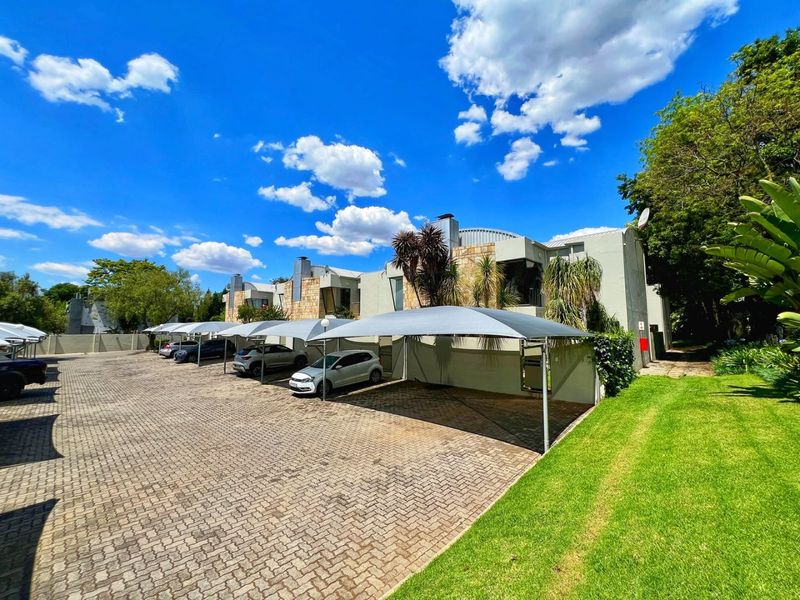 Exterior view of the apartment complex featuring a paved parking area with shade cloth carports and well-maintained lawn.