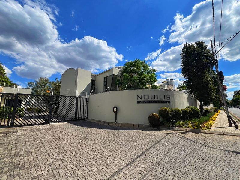 Front exterior view of the Nobilis apartment complex, featuring a paved driveway, secure perimeter wall with electric fencing, and prominent building signage.