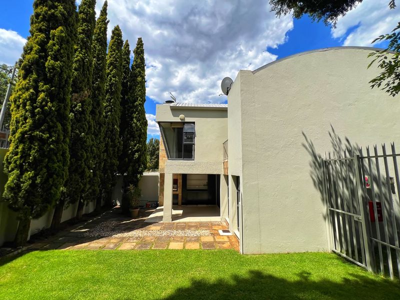 Rear view of the property featuring a paved patio area, landscaped garden, and secure perimeter fencing under a clear sky.
