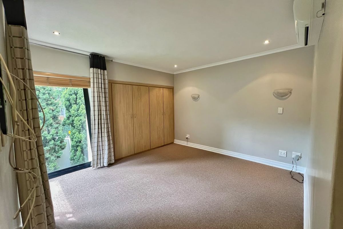 Spacious bedroom featuring neutral carpeting, built-in wooden cupboards, wall-mounted air conditioning, and large sliding glass doors providing natural light.