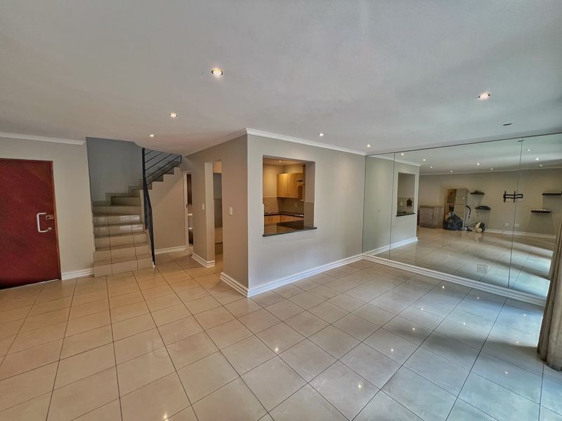 Spacious open-plan living area featuring tiled floors, recessed lighting, a feature mirrored wall, and a convenient pass-through window connecting to the kitchen.