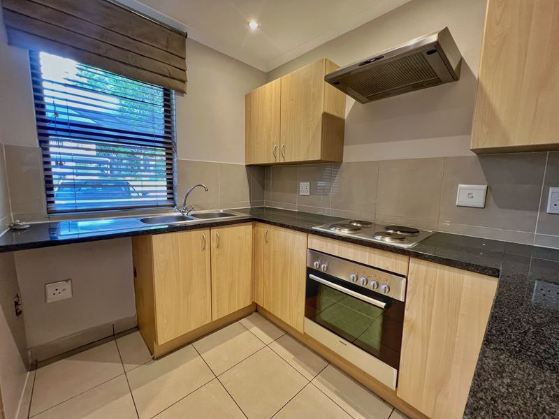 A functional kitchen featuring light wood cabinetry, granite countertops, built-in oven, electric hob, extractor fan, and tiled flooring with a neutral backsplash.