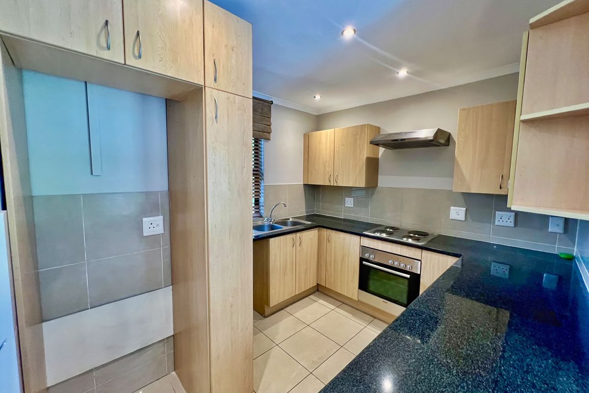 A functional kitchen featuring light wood cabinetry, dark granite countertops, built-in oven, electric hob, extractor fan, and tiled finishes throughout.
