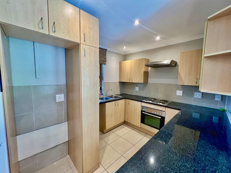 A functional kitchen featuring light wood cabinetry, dark granite countertops, built-in oven, electric hob, extractor fan, and tiled finishes throughout.