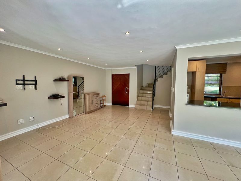 Spacious open-plan living area featuring tiled floors, recessed lighting, a staircase, and a convenient pass-through window connecting to the kitchen.