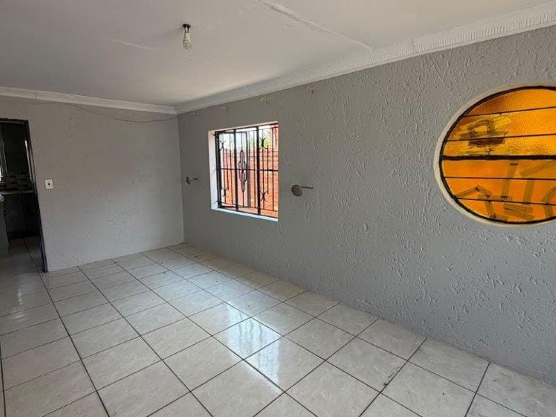 An empty living area featuring tiled floors, a unique circular window, and textured walls, offering a blank canvas for interior design updates.