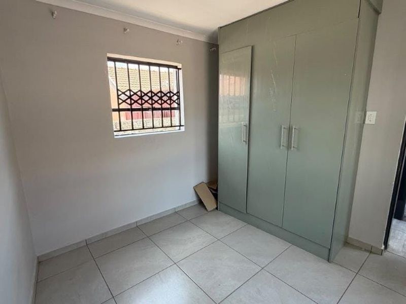 A functional bedroom featuring tiled flooring, a built-in wardrobe, and a window fitted with security bars.