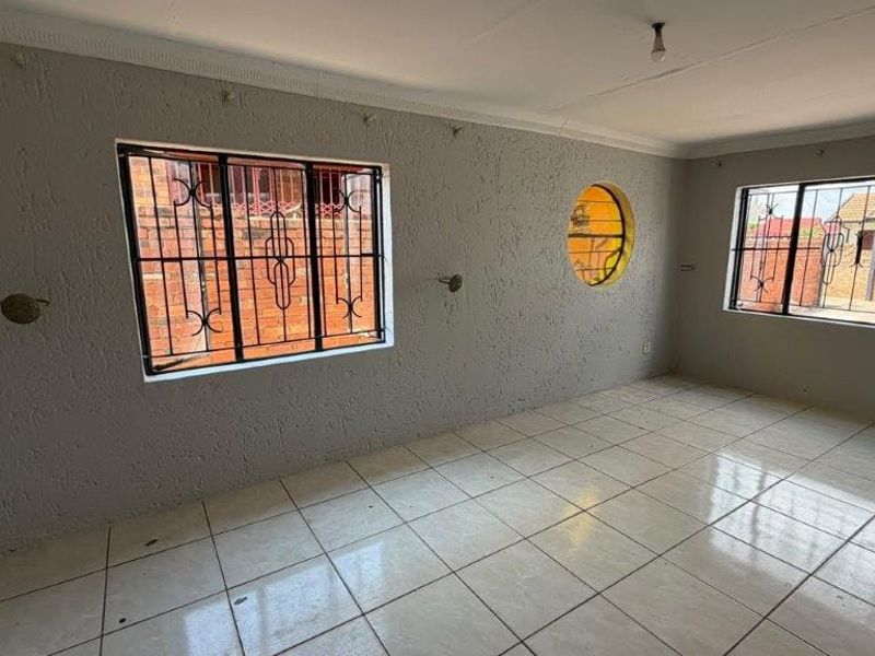 An empty living area featuring tiled flooring, security bars on windows, and a unique circular feature window, awaiting personal touches and interior design.