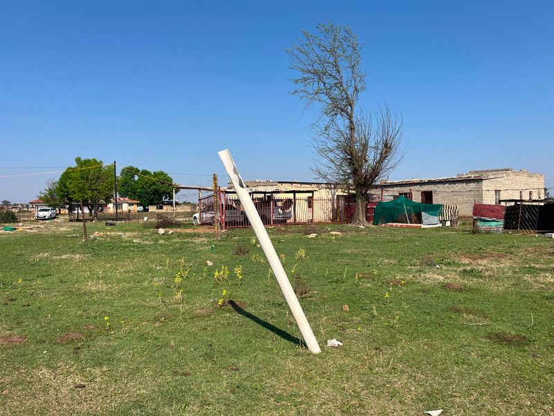 A view of the rear yard area featuring a concrete block structure, perimeter fencing, and an exposed pipe on the property grounds.