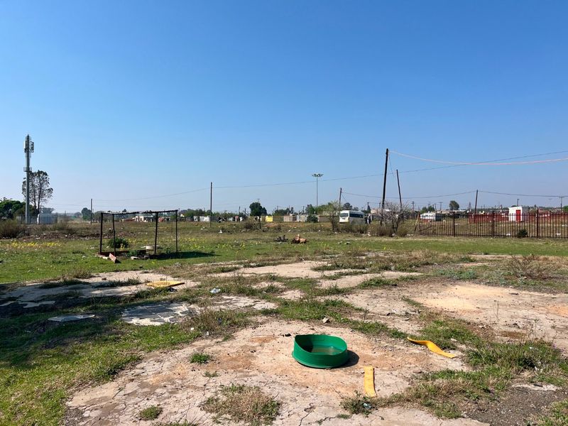 A large, undeveloped plot of land featuring a cracked concrete slab foundation, perimeter fencing, and open field space suitable for future development.